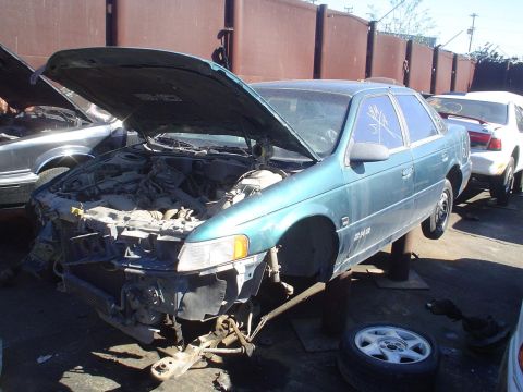 1993 Ford Taurus - Junkyard scene with a 1993 Ford Taurus on lifts and another car behind it.