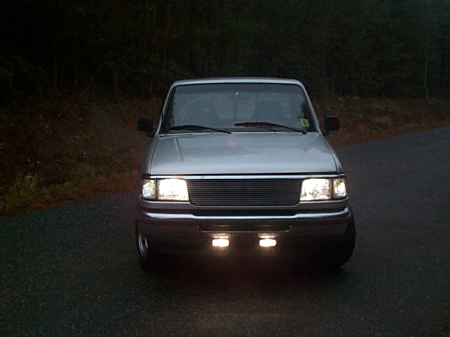 Front view of silver Ford Ranger with billet grille and lit lower driving lights at dusk