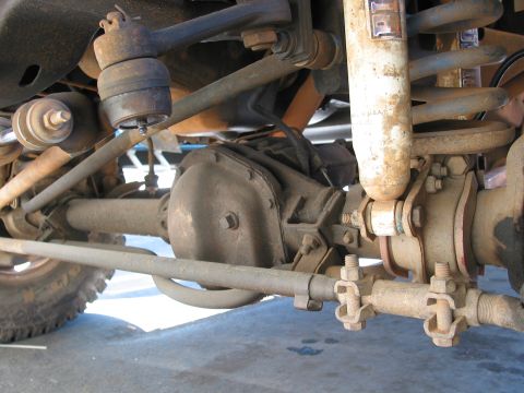 1979 Ford Bronco - Close-up view of the front axle and suspension system, including steering components and a shock absorber.