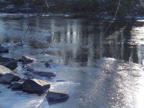 1990 Ford Bronco - A frozen river scene with rocks in the foreground and reflections of trees in the background.