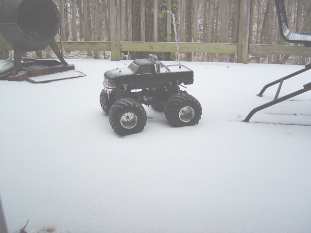 Black toy monster truck in snow, front 3/4 view