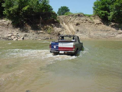1978 Ford Bronco - A truck with the Texas flag painted on its tailgate navigates through a shallow body of water.