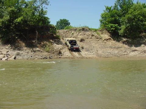 1978 Ford Bronco - A truck navigates a challenging descent down a muddy embankment towards the water's edge.