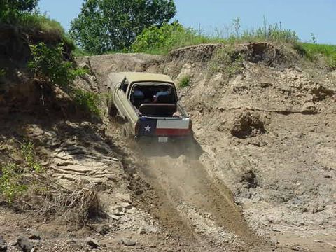 1978 Ford Bronco - A tan 1978 Ford Bronco navigates a steep dirt incline, displaying the Texas flag on its rear.