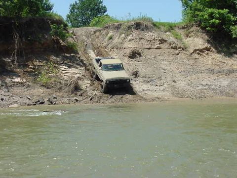 1978 Ford Bronco - This 1978 Ford Bronco navigates a challenging off-road terrain, ascending a muddy incline beside a river.