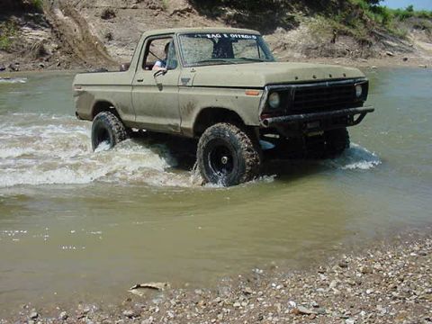 1978 Ford Bronco - A tan Ford F-Series truck navigates through a shallow river, kicking up water.
