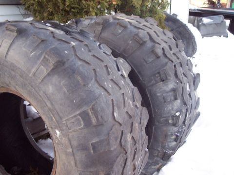 1974 Ford Bronco - Several large, knobby tires are stacked outdoors in a snowy environment.