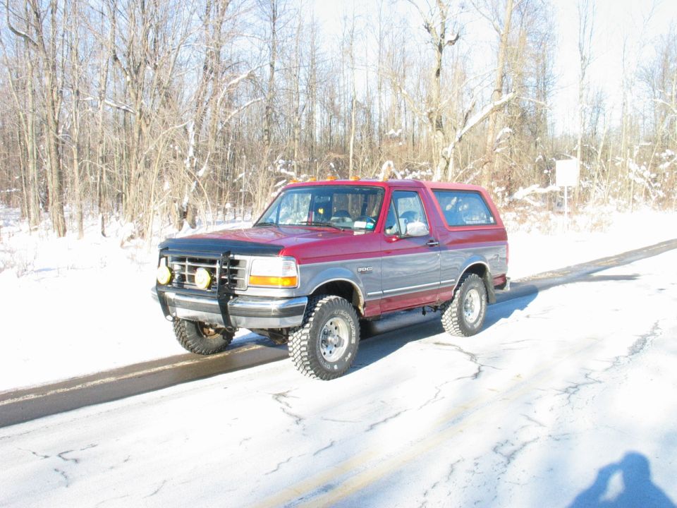 1995 Ford Bronco parked on a snow-covered road with trees in the background