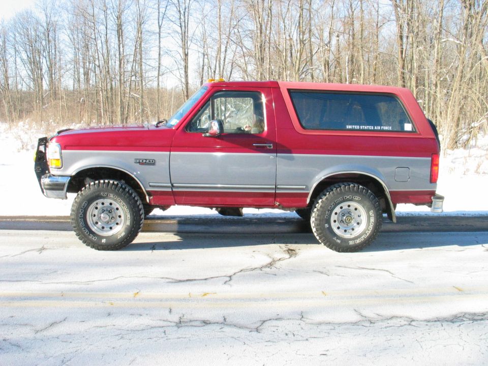 Red and silver two-tone Ford Bronco in profile on a snowy road with brush guard and all-terrain tires