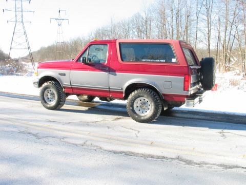 1995 Ford Bronco - This red and silver Ford Bronco is seen from the rear quarter angle, with a spare tire mounted on the back.