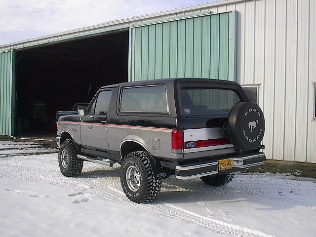 1989 Ford Bronco parked in front of a barn in the snow, rear view with spare tire mounted