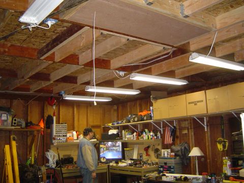 1989 Ford Bronco - A cluttered garage workshop with fluorescent lights and shelves filled with items.