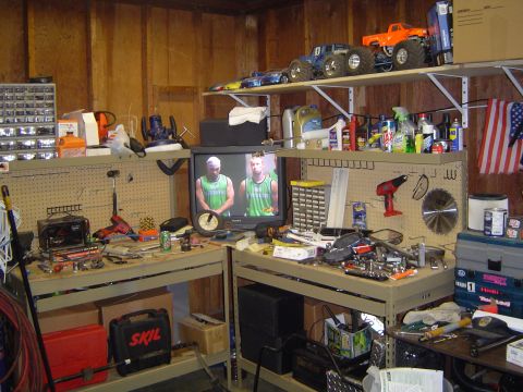 1989 Ford Bronco - A cluttered garage scene displays workbenches laden with tools, storage units, and a television set.