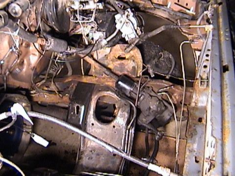 1990 Ford Bronco - Grimy engine bay shot down onto a partially disassembled engine compartment, showing a rusty inner fender and shock tower, ignition coil, b…