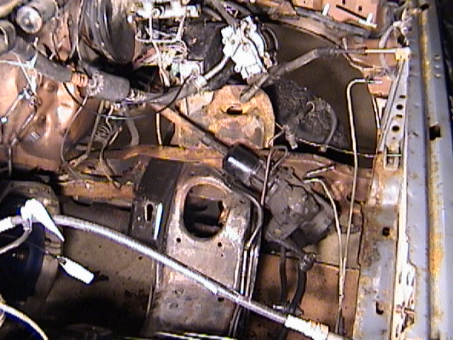 Dirty partially disassembled engine bay with rusty shock tower, coil and wiring