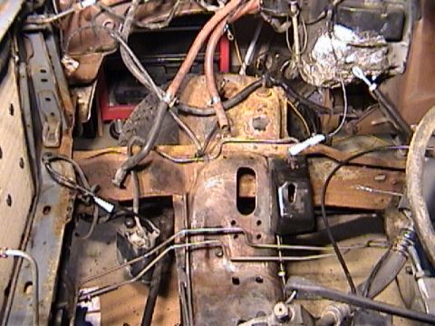 1990 Ford Bronco - Engine bay with the engine pulled, looking down at a rusty, grease-caked shock tower and inner fender with brake and fuel hard lines, heate…