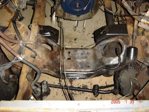 1990 Ford Bronco - Overhead view down into a stripped engine bay with the engine removed, showing the bare crossmember, front differential housing, radius arm…