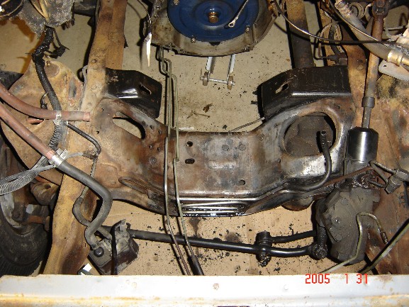 Overhead view of stripped engine bay showing bare frame, front axle and coil springs