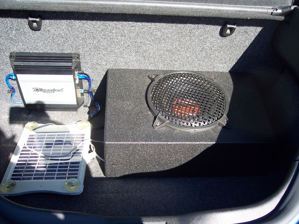 Car trunk with custom subwoofer box, Directed amplifier, blue wiring, and a small solar panel
