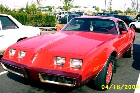 1979 Pontiac Firebird - A red 1979 Pontiac Firebird is parked in a lot, showing its distinctive front end and side profile.