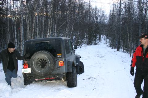 2003 Jeep TJ - A Jeep TJ is stuck in the snow, with one person attempting to free it while another observes.