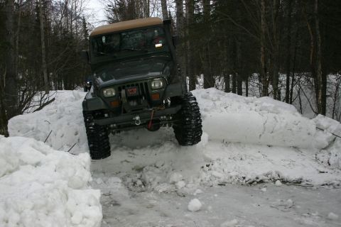2003 Jeep TJ - A green 2003 Jeep TJ navigates a snowy obstacle course in a wooded area.