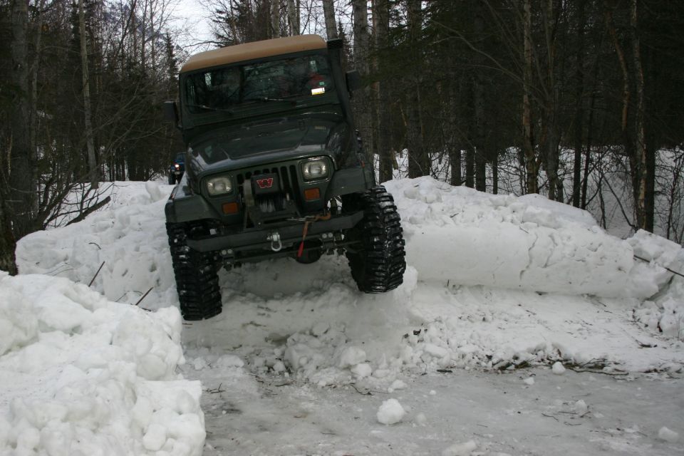 Green 2003 Jeep TJ driving over snowbank