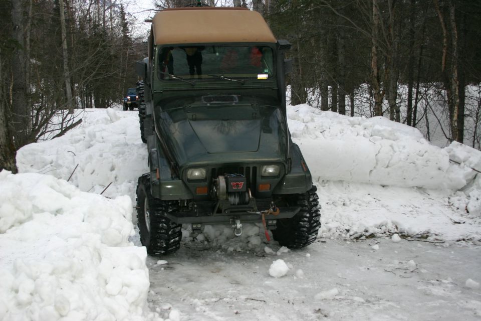 Green 2003 Jeep TJ driving on a snow-covered road with another vehicle behind it