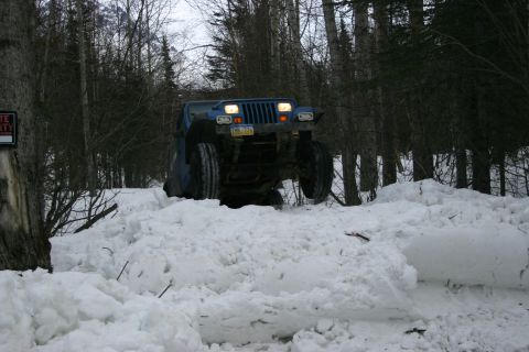 2003 Jeep TJ - A blue Jeep Wrangler navigates a snow-covered path, with its front tires high in the air.