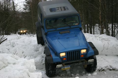 2003 Jeep TJ - A blue Jeep Wrangler navigates a snowy path, with another vehicle visible in the distance.