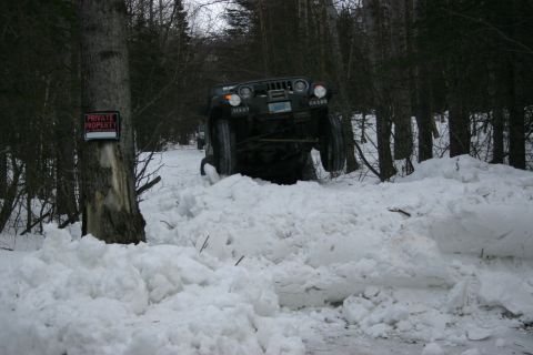 2003 Jeep TJ - A dark green Jeep Wrangler TJ navigates a snow-covered path, its front end visible as it gets stuck.