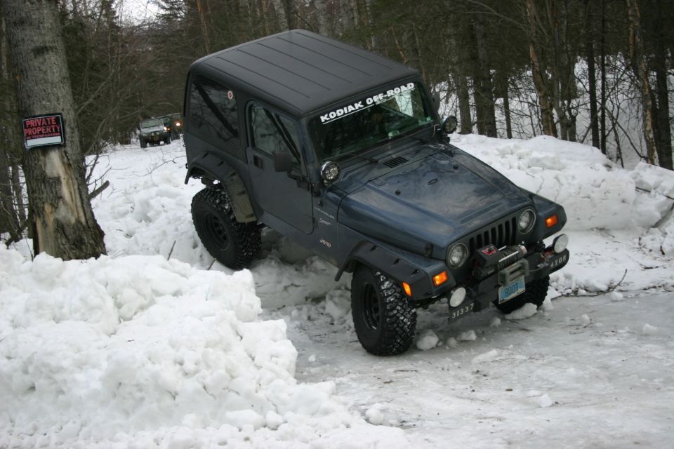 Dark blue Jeep Wrangler TJ with 'KODIAK OFF-ROAD' sticker on windshield driving through snow, another Jeep visible in background