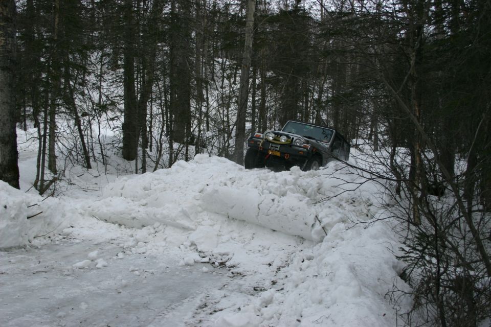 Jeep TJ driving through a deep snow drift on a wooded trail. It's a 2003 Jeep TJ