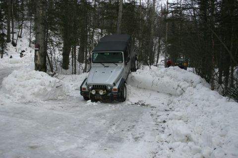 2003 Jeep TJ - A silver Jeep Wrangler navigates a snow-covered path, with another vehicle visible in the background.