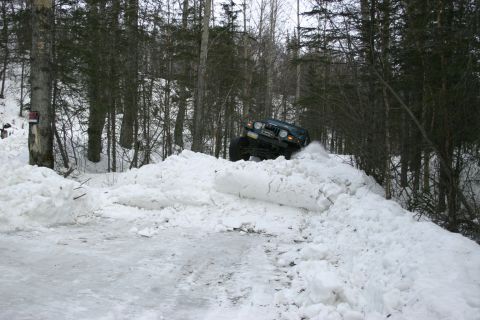 2003 Jeep TJ - A 2003 Jeep TJ navigates a steep snowbank on a winter trail surrounded by trees.