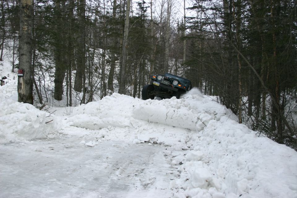 Dark green 2003 Jeep TJ climbing a snowdrift on a wooded trail