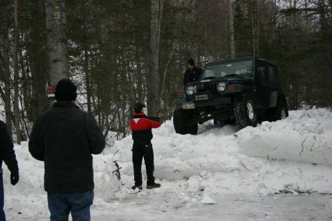 2003 Jeep TJ - A dark green Jeep TJ is partially buried in a snowdrift with people nearby.