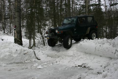 2003 Jeep TJ - A dark green Jeep Wrangler navigates a snowy trail in a forest.