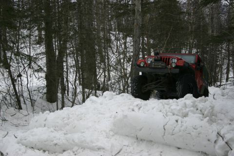 2003 Jeep TJ - A red 2003 Jeep TJ Wrangler navigates a snow-covered trail, demonstrating its off-road capabilities.