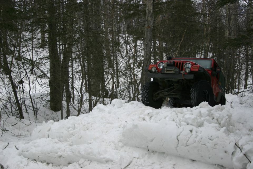 Red 2003 Jeep TJ Wrangler driving through deep snow, front 3/4 view