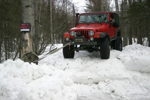 2003 Jeep TJ - Red Jeep TJ winching itself out of deep snow in a wooded area.