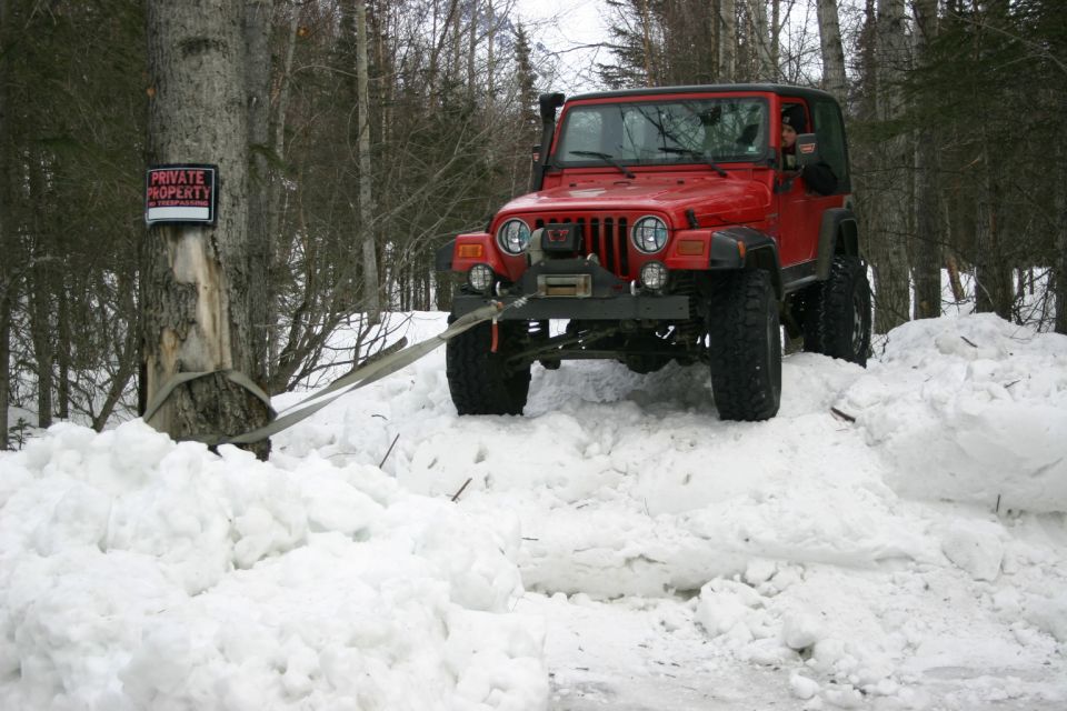 Red Jeep TJ with winch in snow, pulling itself with a strap around a tree