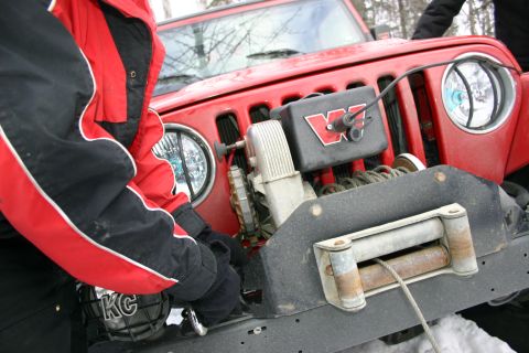 2003 Jeep TJ - A person in a red jacket works on the winch of a red Jeep Wrangler in a snowy environment.