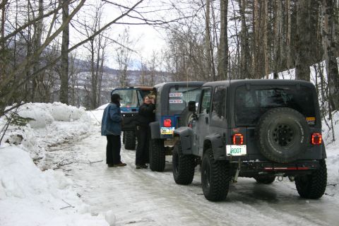 2003 Jeep TJ - Multiple Jeep Wranglers are parked in a line on a snow-covered road, with trees lining the background.