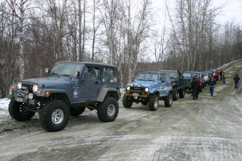 2003 Jeep TJ - A line of off-road vehicles, led by a blue 2003 Jeep TJ, travels down a snowy road.
