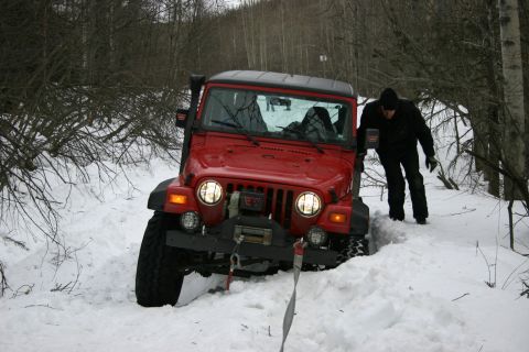 2003 Jeep TJ - A red Jeep TJ is partially buried in snow, with a person standing next to it in a wooded area.