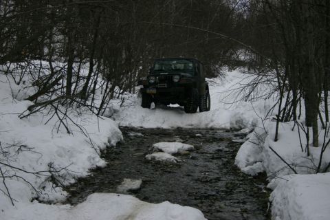 2003 Jeep TJ - A dark green Jeep Wrangler navigates a snowy creek bed, demonstrating its off-road capability in winter conditions.