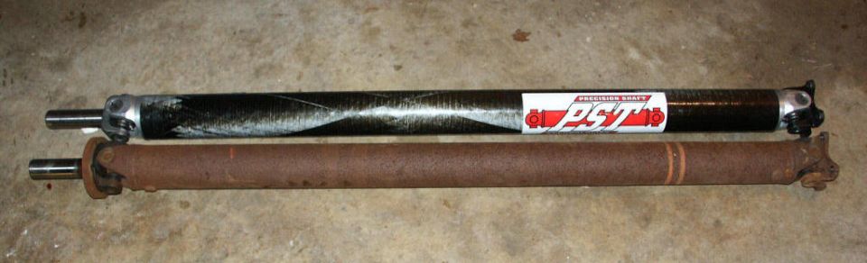 Two driveshafts on garage floor, one with red Precision Shaft sticker beside an older rusty one