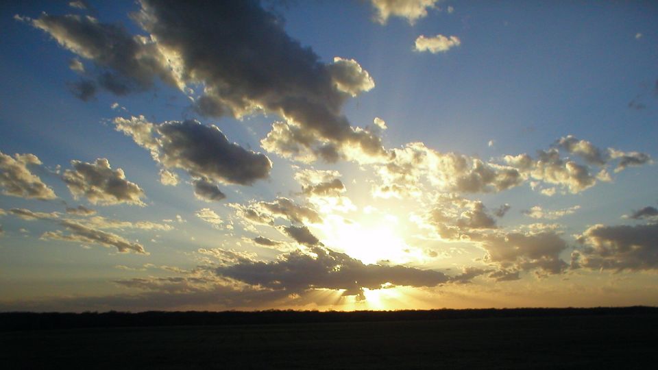 Sunset over flat open horizon with scattered clouds and sun rays through the gaps