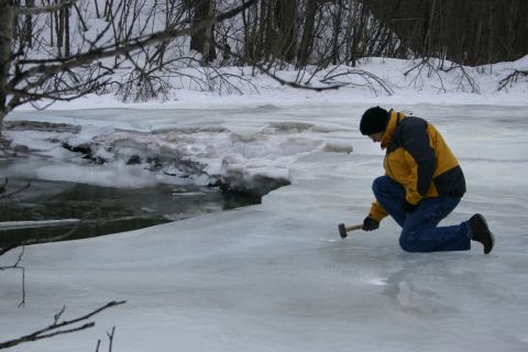 2003 Jeep TJ - A person kneels on a frozen surface, examining the ice with a hammer.